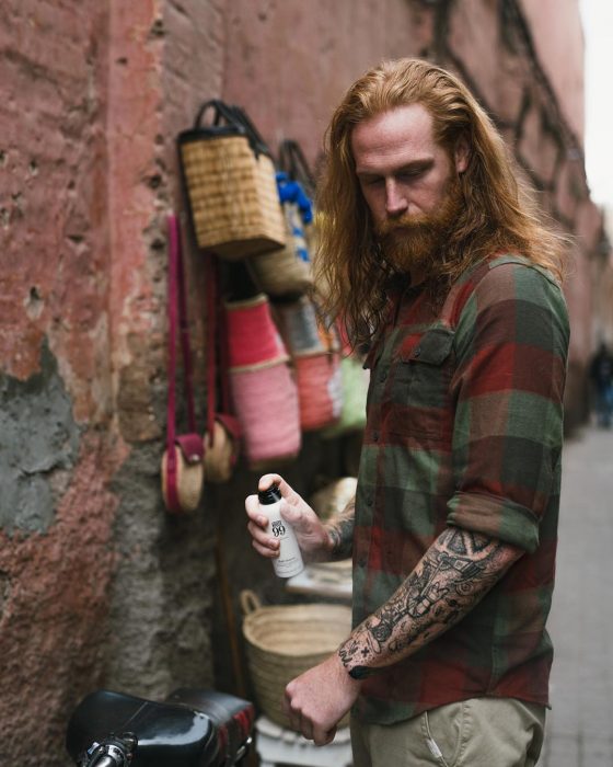 Gwilym C. Pugh, modelo y fotógfrafo, hombre pelirrojo con cabello largo, barba y bigote tupido, con camisa de cuadros y tatuajes en los brazos