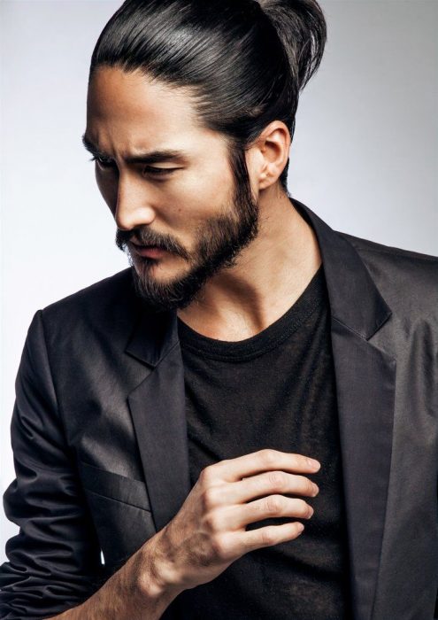 Tony Thornburg, modelo y actor hawaiano de cabello negro, lacio y largo agarrado en man bun, con barba y bigote corto, con saco negro y playera casual