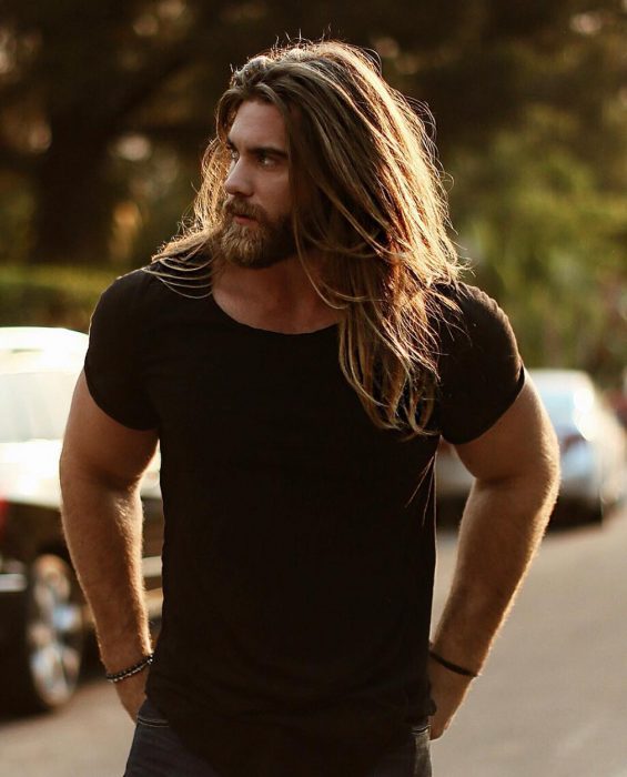 Modelo Brock O'Hurn, hombre musculoso con camisa negra, de cabello largo y castaño, con barba y bigote tupidos 