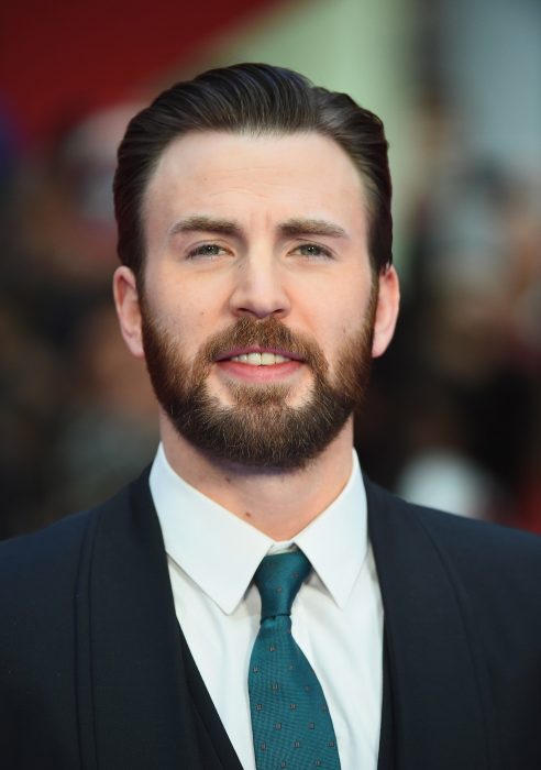 Actor Chris Evans, hombre con cabello corto y peinado para atrás, con barba y bigote poblado, ojos verdes, con traje de gala y corbata verde aqua