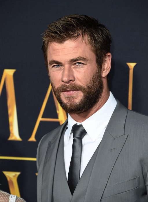 Actor Chris Hemsworth, hombre de cabello corto y rubio, con barba y bigotes tupidos, ojos azules, vestido con traje de gala gris