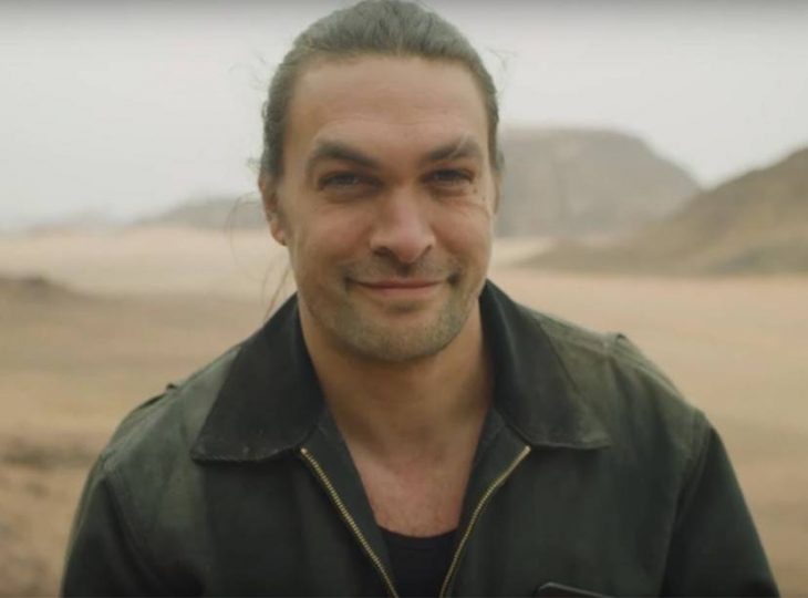 Jason Momoa llevando chaqueta de cuero, sonriendo a la cámara para una fotografía después de afeitar su barba 