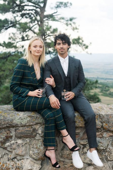 Joe jonas y Sophie turner sentados en una barda con una bebida en la mano