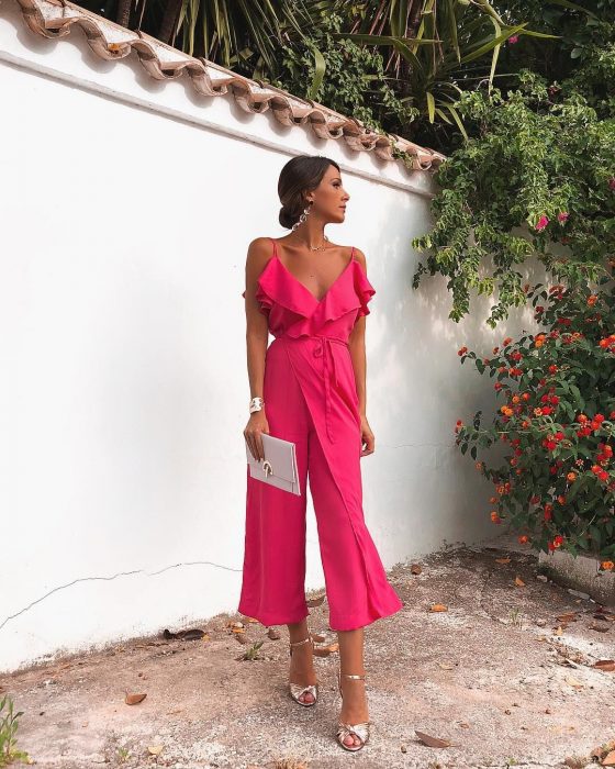 Chica usando un jumpsuit de color rosa con zapatos y accesorios plateados mientras posa para una foto durante una sesión en un jardín 