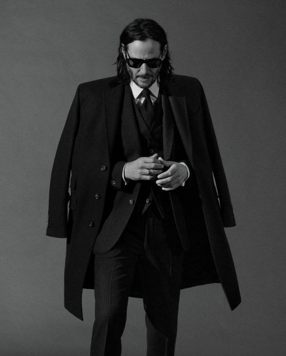 Keanu Revees usando traje sastre en color negro, con las manos unidas, modelando un abrigo, GQ, Jhon Wick: Parabellum