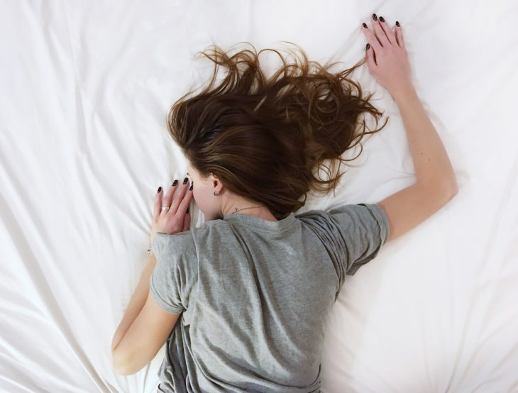 Chica con blusa gris, recostada boca abajo, sobre una cama con sabanas blancas, haciendo prueba para entrar a La NASA y ganar 19 mil dólares