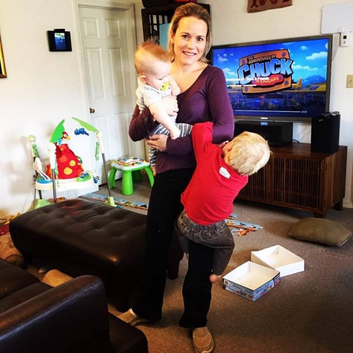 Celeste Erlach: Carta de esposa exhausta a su esposo; mamá cargando a dos niños en un cuarto con juguetes y la televisión en un canal para infantil
