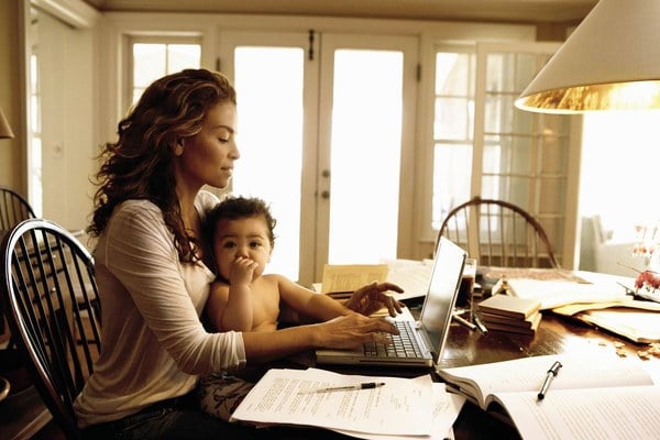 Mamá joven cargando a su bebé mientras trabaja en laptop