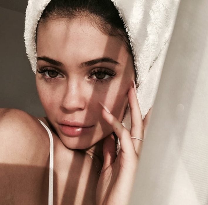 Chica llevando toalla sobre la cabeza, acariciando su rostro y modelando para una selfie en el baño