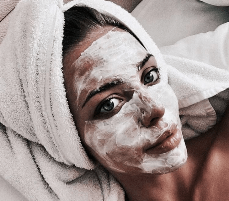 Chica recostada sobre su cama llevando mascarilla facial para limpiar la piel 