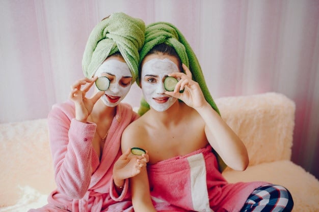 Amigas usando mascarillas refrescantes y rodajas de pepino sobre los ojos