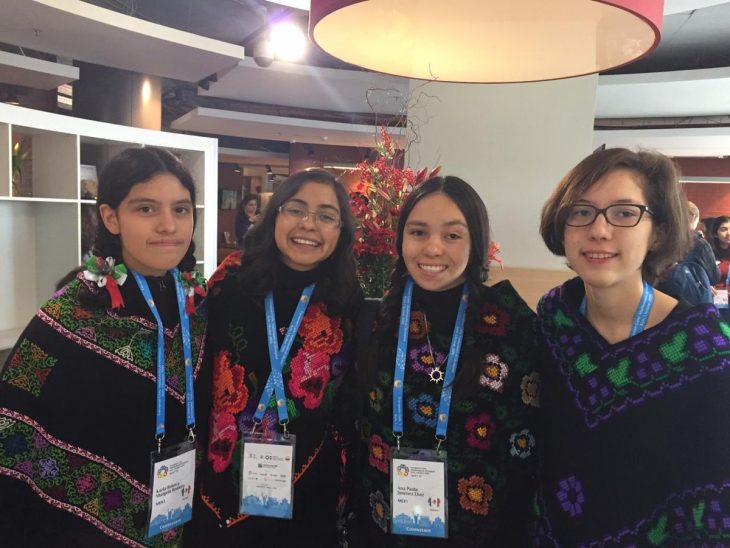 Chicas usando sudaderas con detalles de flores bordados, gafete con correa azul, dentro se la sala de premiación de la sala de Olimpiada Europea Femenil en matemáticas ,Ana Paula Jiménez, Nuria Sydykova Méndez y Karla Rebeca Munguía Romero