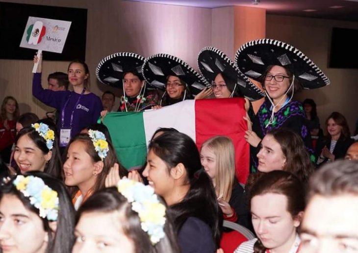 Ana Paula Jiménez, Nuria Sydykova Méndez y Karla Rebeca Munguía Romero usando sombreros charros con detalles plateados sosteniendo una bandera mexicana durante las olimpiadas europeas femenil en matemáticas 