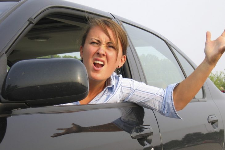 Mujer dentro de un auto con la cabeza y el brazo afuera reclamando enojada