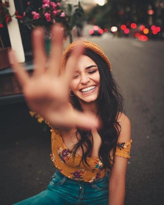 Mujer sentada en la calle tapándose la cara mientras le toman una foto