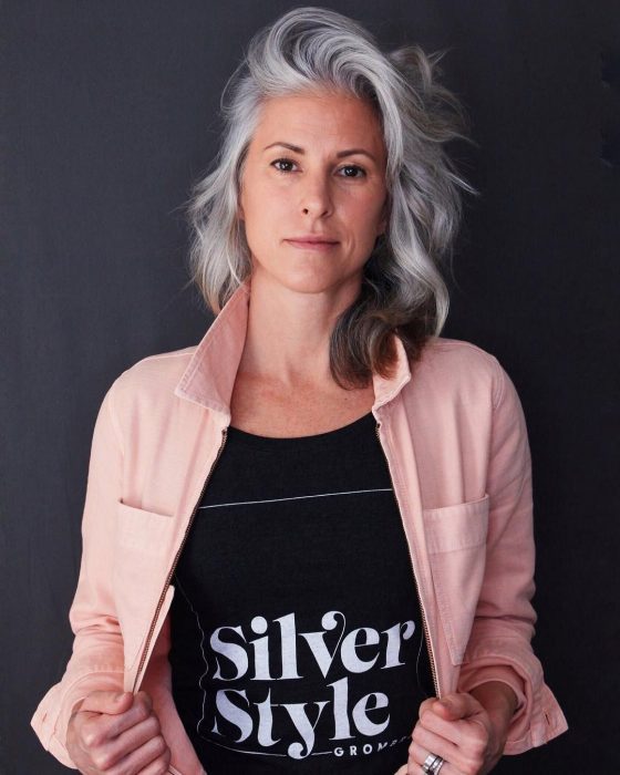 Mujer con canas con una blusa negra que dice Silver Style y una chamarra de mezclilla rosa