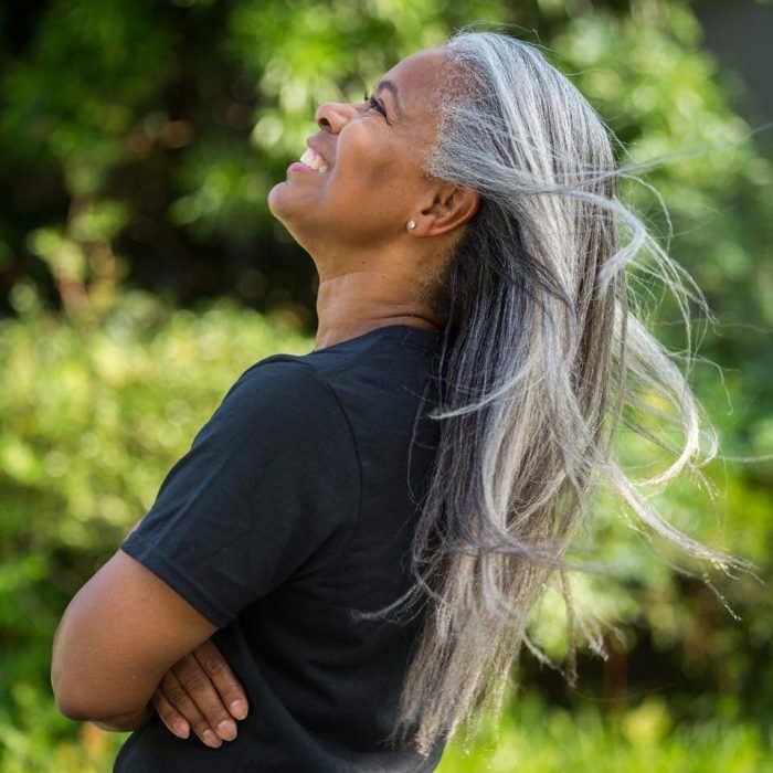 Mujer afroamericana posando de perfil y sonriendo, cabello largo, lacio y con canas