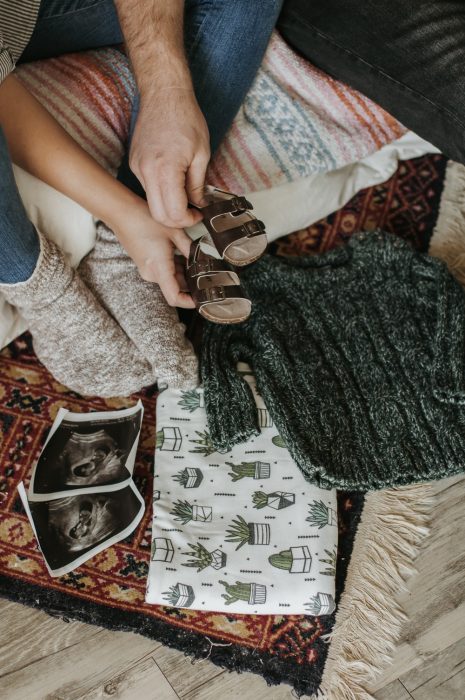 Couple of spouses showing ultrasounds of their next baby, clothes for a child, baby sandals