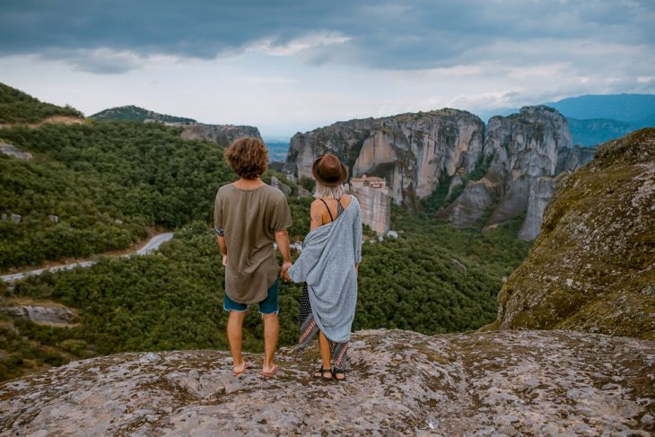 Pareja de novios tomados d elas manos sobre la cima de una montaña admirando el panorama del bosque