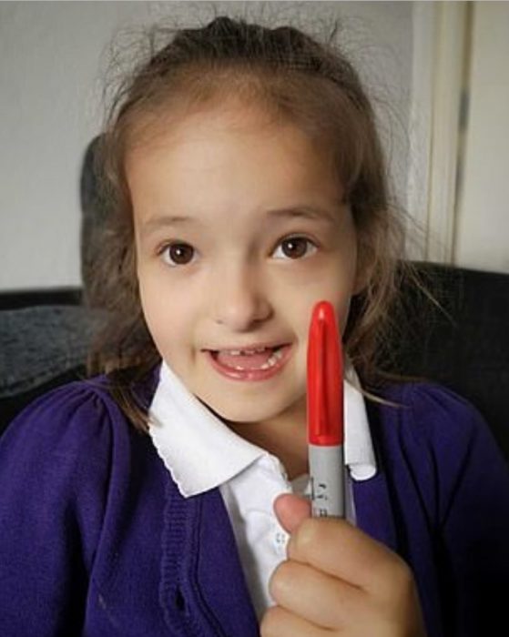 Lily Schooley, niña pequeña con uniforme escolar sosteniendo un plumón rojo