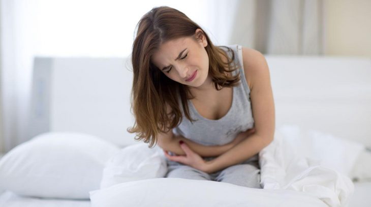 chica sentada en la orilla de una cama con dolor abdominal intenso