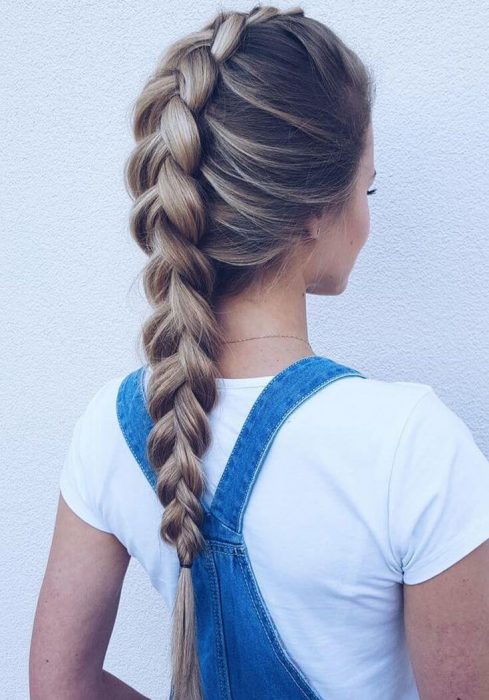 Chica de espaldas con top blanco y overol azul con una trenza invertida