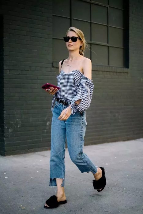 Girl walking down the street with cell phone in her hand while wearing jeans, peasant and some hairy sandals 