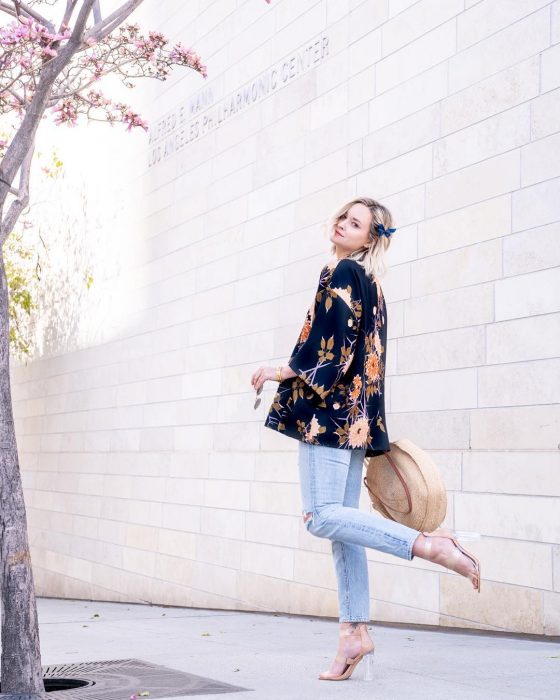 Chica caminando por la calle mostrando sus zapatillas con transparencias, jeans, abrigo y sombrero 