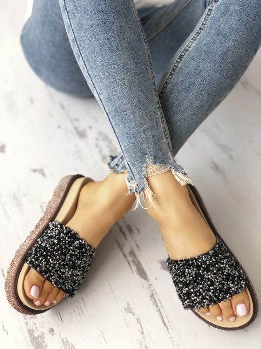 Feet of a girl wearing jeans and black sandals with sparkles 