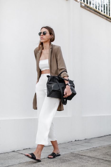 Girl wearing a white outfit with a brown cardigan, black bag and black sandals while walking down the street 