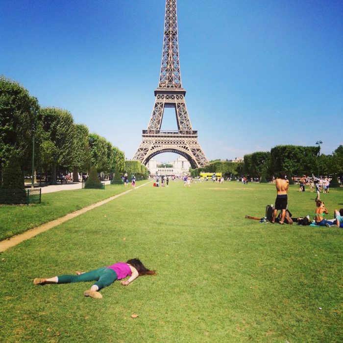 STEFDIES, la chica que se ha vuelto viral por sus antiselfies, selfie de mujer con clusa rosa frente a la Torre Eiffel con turistas alrededor en el pasto