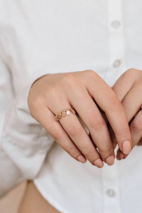 Mujer mostrando sus manos delgadas que portan un anillo dorado con piedras colgantes