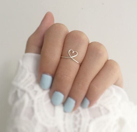 Mujer mostrando su mano con uñas en tono azul y anillo en forma de corazón al centro 