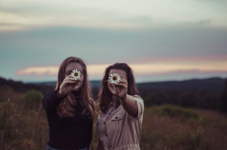 Tipo de amiga Acuario, chicas a mitad del campo en pleno atardecer sosteniendo un par de margaritas en sus manos mientras las fotografían 