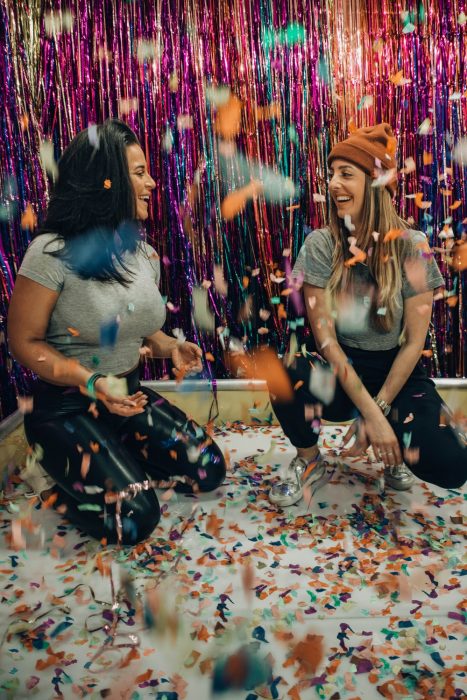 Tipo de amiga Leo, chicas inclinadas en cuclillas dentro de una habitación decorada con confeti y papel de colores 