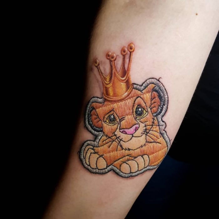 Tatuaje bordado del Rey León de Disney en el brazo, de tatuador brasileño Eduardo "Duda" Lozano