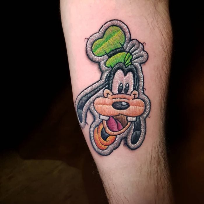 Tatuaje bordado de Goofy en el brazo, de tatuador brasileño Eduardo "Duda" Lozano