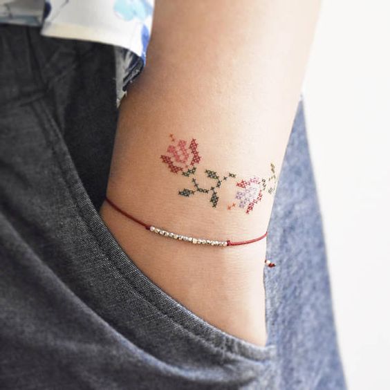 Chica modelando su muñeca tatuada con pequeñas rosas con efecto bordado en punto de cruz