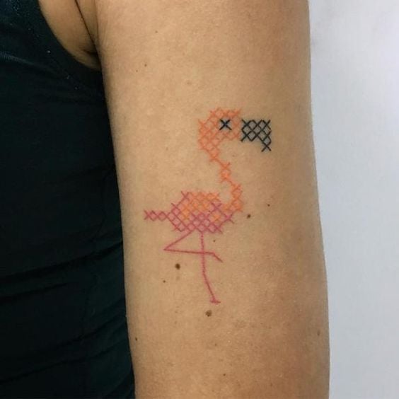 Persona mostrando su brazo tatuado con un flamingo de color naranja con efecto de bordado en punto de cruz