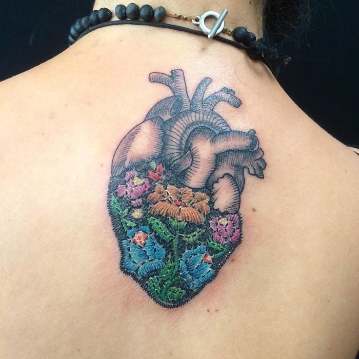 Persona volteada de espaldas mostrando su espalda tatuada con un diseño de corazón humano con efecto bordado 