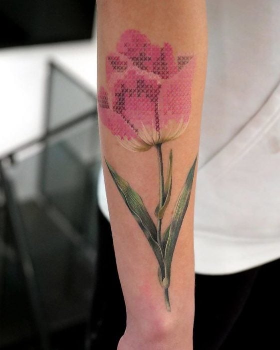 Persona mostrando su ante brazo con un tatuaje de tulipán rosa con efecto bordado en punto de cruz