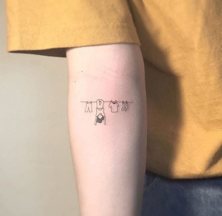 Tatuaje pequeño de un tendedero de ropa con una chica en el brazo