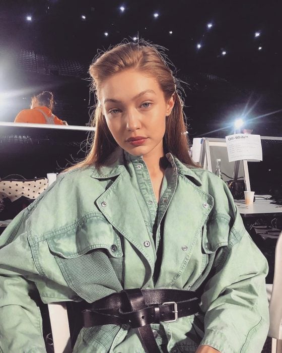 Model Gigi Hadid, girl with brown blond hair and bluish gray eyes, with big green jacket with belt as dress, oversized trend