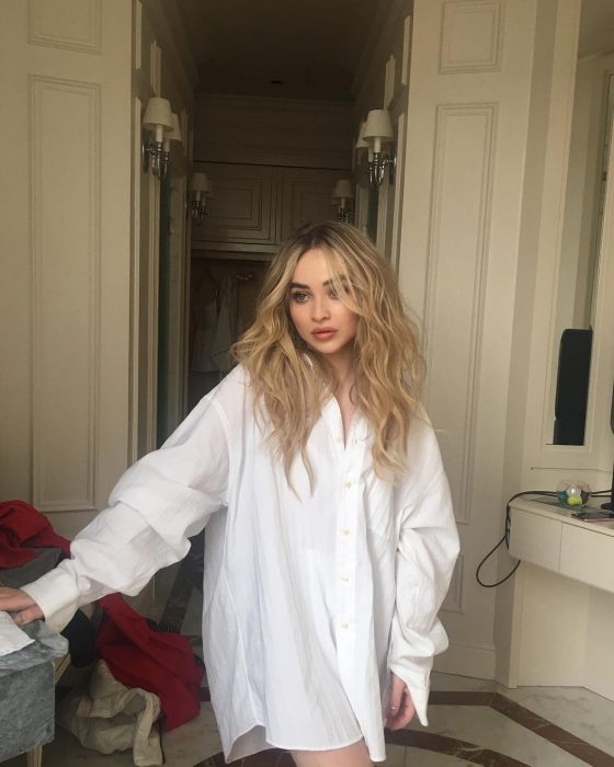 Actress Sabrina Carpenter, blonde, long wavy girl wearing a large white shirt, oversized trend