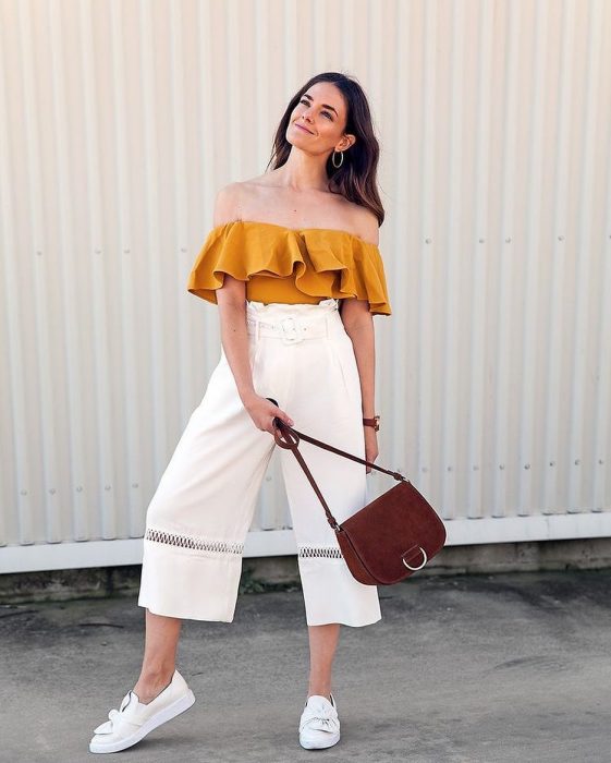 Chica modelando un pantalón holgado blanco con bodie de hombros caídos color amarillo con bolsa café