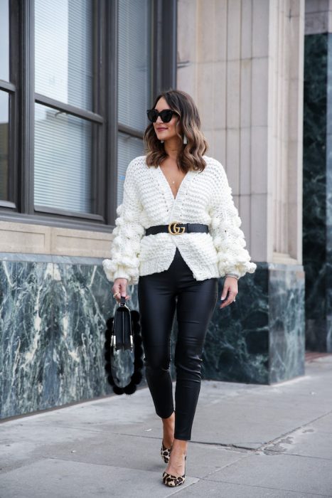 Chica caminando por la calle con saco blanco y cinturón negro, leggin negro, bolsa grande negra y lentes oscuros