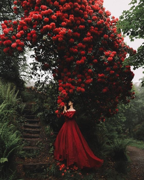 Vestidos de novia vintage confeccionados por la diseñadora Joanne Fleming, mujer bajo un gran árbol de bugambilias rojas, con vestido frondoso color rojo sin hombros