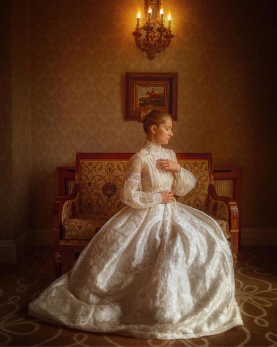 Vestidos de novia vintage confeccionados por la diseñadora Joanne Fleming, mujer con peinado chongo sentada en un sillón antiguo, usando vestido frondoso blanco de encaje, con mangas y cuello con botones