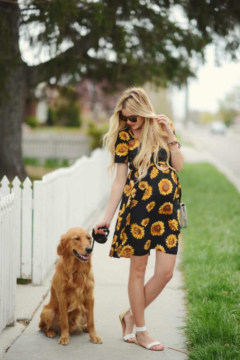 Vestidos para baby shower, mujer de cabello largo y rubio despeinado, paseando a perro golden retriever dorado, con vestido negro con girasoles y sandalias blancas