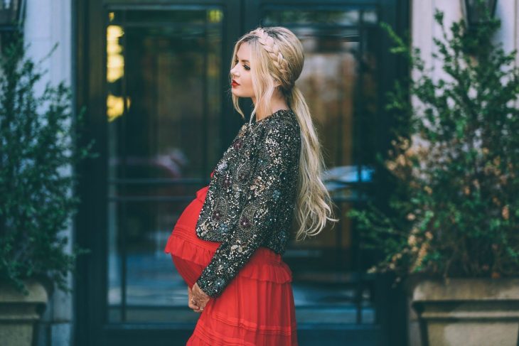 Vestidos para baby shower, mujer con vestido rojo y saco de pedrería en sesión de fotos de maternidad, peinado para cabello largo con corona de trenza y una coleta